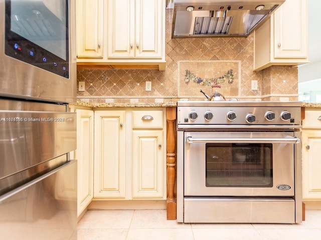 kitchen featuring range hood, light stone counters, stainless steel appliances, backsplash, and light tile patterned floors