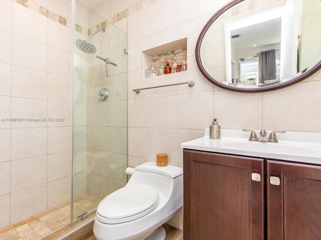 bathroom with vanity, tile walls, toilet, a shower with door, and decorative backsplash