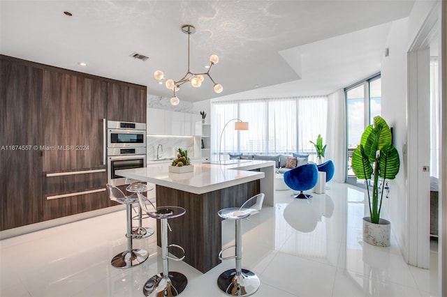 kitchen with light tile patterned flooring, a kitchen island, backsplash, a kitchen breakfast bar, and stainless steel double oven