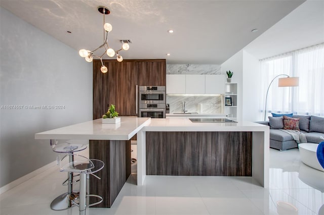 kitchen with tasteful backsplash, double oven, white cabinets, pendant lighting, and a kitchen breakfast bar