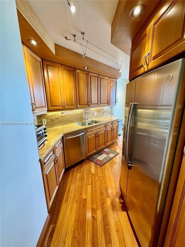 kitchen with light wood-style flooring, a sink, appliances with stainless steel finishes, tasteful backsplash, and brown cabinetry