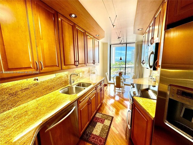 kitchen featuring backsplash, appliances with stainless steel finishes, light stone countertops, light hardwood / wood-style floors, and sink