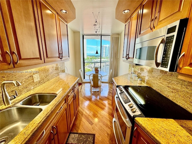 kitchen with appliances with stainless steel finishes, a sink, expansive windows, light wood-type flooring, and backsplash