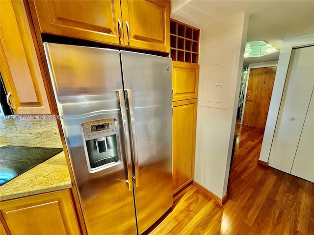 kitchen with wood finished floors, brown cabinetry, stainless steel fridge, and light stone countertops