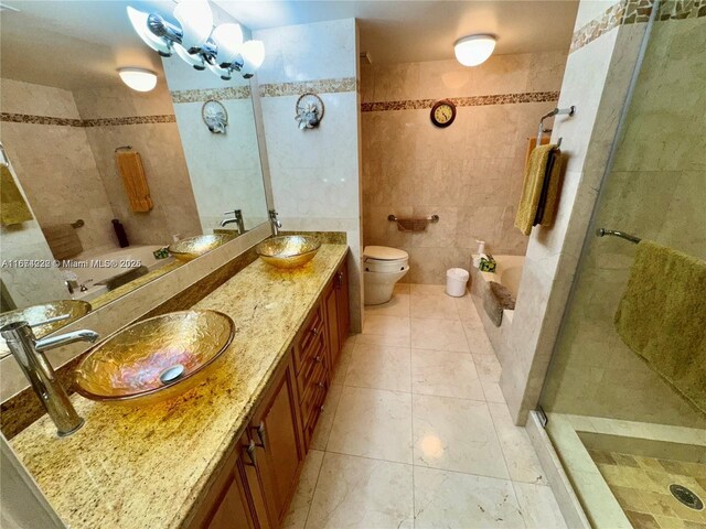 bathroom with an inviting chandelier, tile walls, toilet, vanity, and an enclosed shower