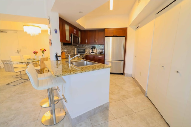 kitchen with kitchen peninsula, decorative backsplash, appliances with stainless steel finishes, a breakfast bar, and sink