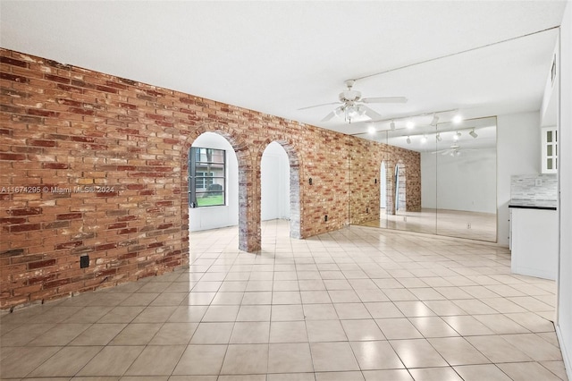 unfurnished room featuring track lighting, light tile patterned floors, ceiling fan, and brick wall