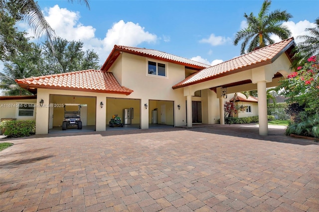 rear view of property featuring decorative driveway, a tiled roof, and stucco siding