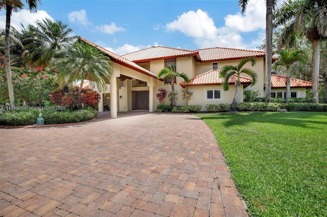 mediterranean / spanish-style house with decorative driveway, a front yard, a tile roof, and stucco siding