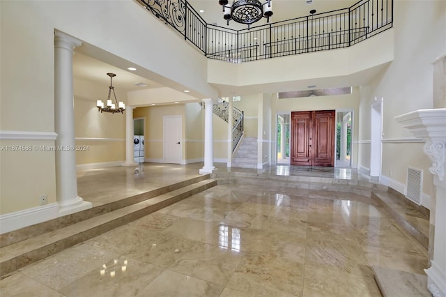 foyer entrance with a high ceiling, a notable chandelier, ornate columns, and washer / clothes dryer