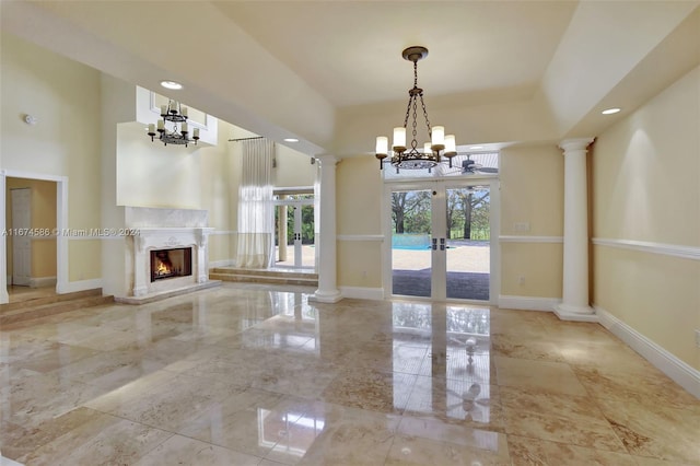 unfurnished living room with decorative columns, a notable chandelier, a fireplace, and french doors