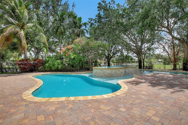 view of pool with a patio area, fence, and a pool with connected hot tub