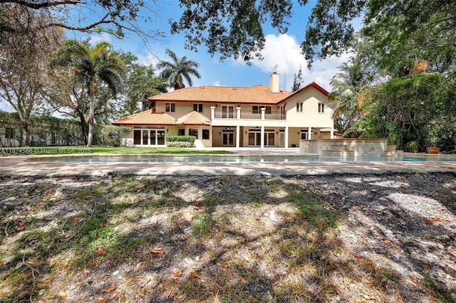 rear view of house with a tile roof, an outdoor pool, a chimney, and a balcony