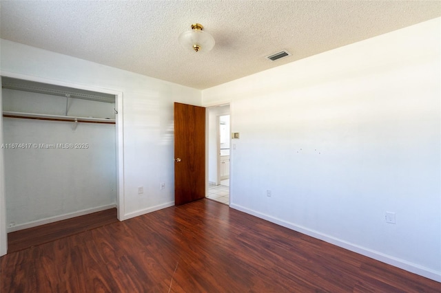 unfurnished bedroom featuring a textured ceiling, dark hardwood / wood-style flooring, and a closet