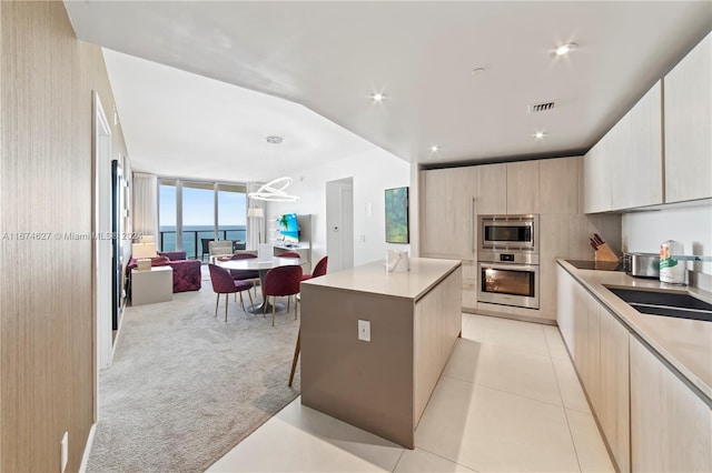 kitchen with hanging light fixtures, appliances with stainless steel finishes, a center island, light colored carpet, and a water view