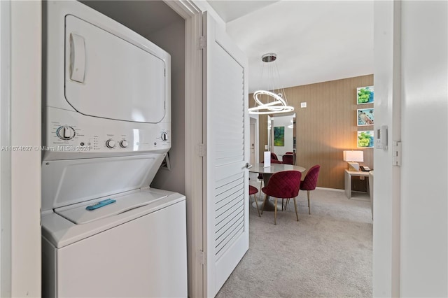 clothes washing area featuring light carpet, stacked washer / dryer, and a chandelier