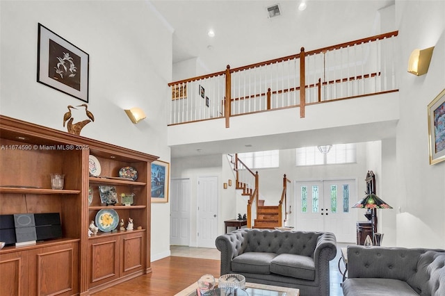 living room featuring light wood-type flooring, a towering ceiling, and french doors