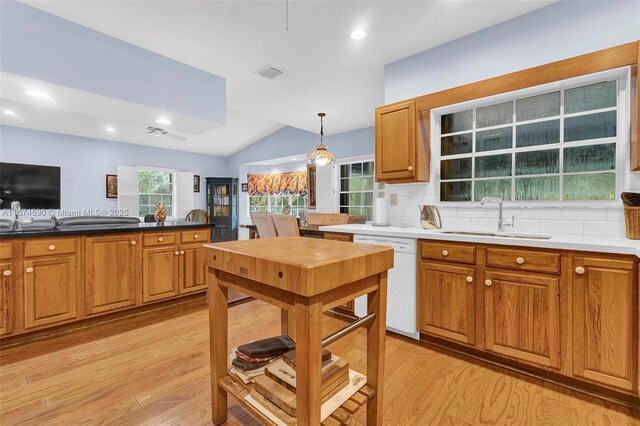 kitchen with decorative backsplash, white dishwasher, sink, pendant lighting, and lofted ceiling