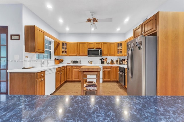 kitchen with appliances with stainless steel finishes, backsplash, ceiling fan, sink, and light hardwood / wood-style floors