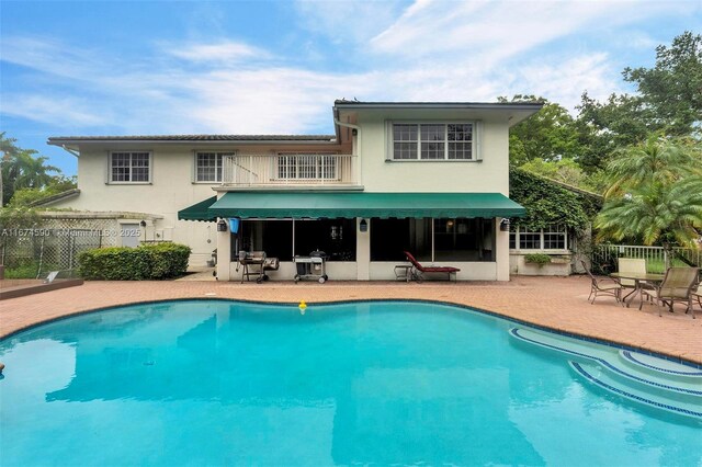 rear view of house with a patio, a fenced in pool, and a balcony