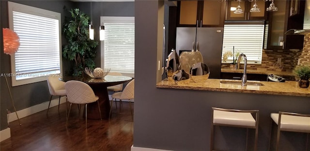 kitchen with light stone counters, dark hardwood / wood-style floors, stainless steel fridge, sink, and decorative light fixtures