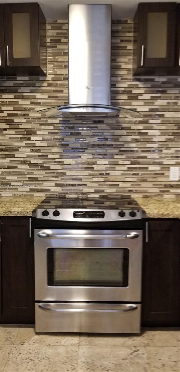 kitchen featuring stainless steel fridge, dark brown cabinets, light stone countertops, and backsplash