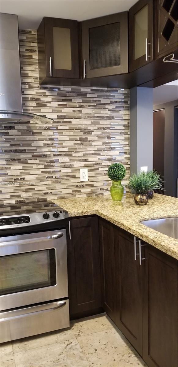 kitchen with decorative backsplash, light stone countertops, dark brown cabinetry, and stainless steel range oven