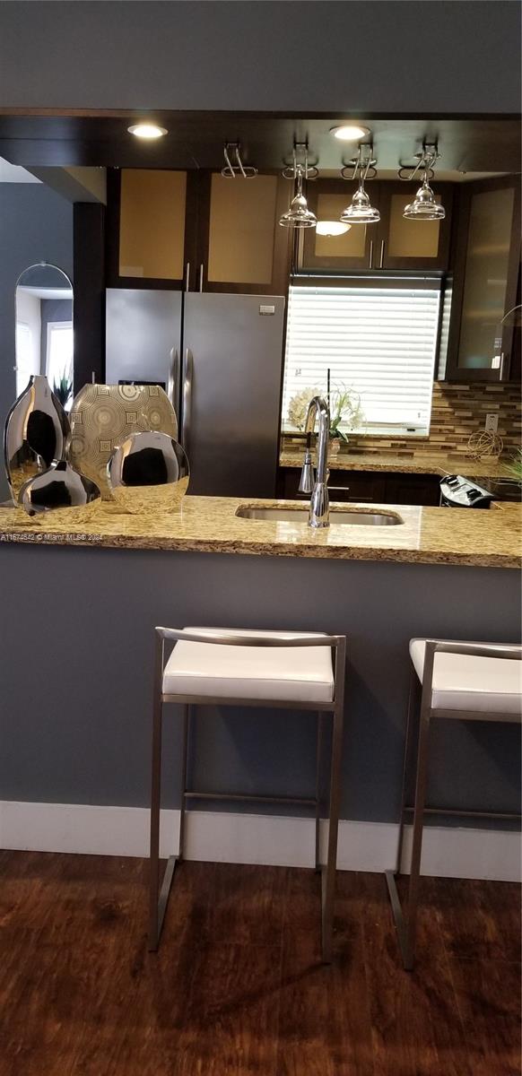 kitchen with backsplash, dark brown cabinetry, light stone counters, and sink