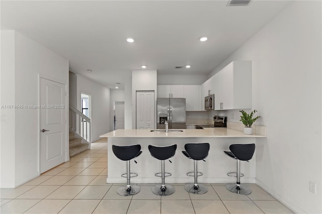 kitchen with kitchen peninsula, appliances with stainless steel finishes, white cabinets, and a kitchen breakfast bar