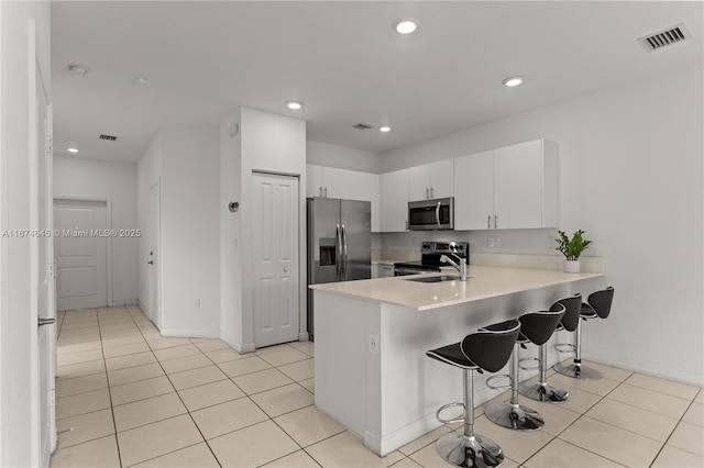 kitchen with white cabinets, sink, appliances with stainless steel finishes, a kitchen bar, and kitchen peninsula