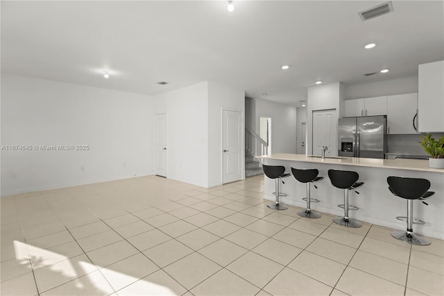 kitchen featuring a breakfast bar, stainless steel refrigerator with ice dispenser, white cabinetry, and light tile patterned flooring