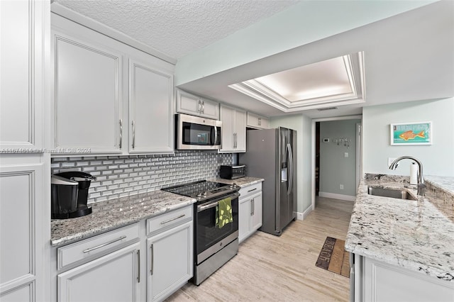 kitchen with sink, light stone counters, light hardwood / wood-style floors, white cabinets, and appliances with stainless steel finishes