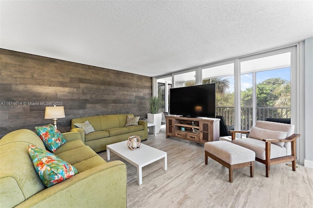 living room featuring floor to ceiling windows, a textured ceiling, light hardwood / wood-style flooring, and wood walls