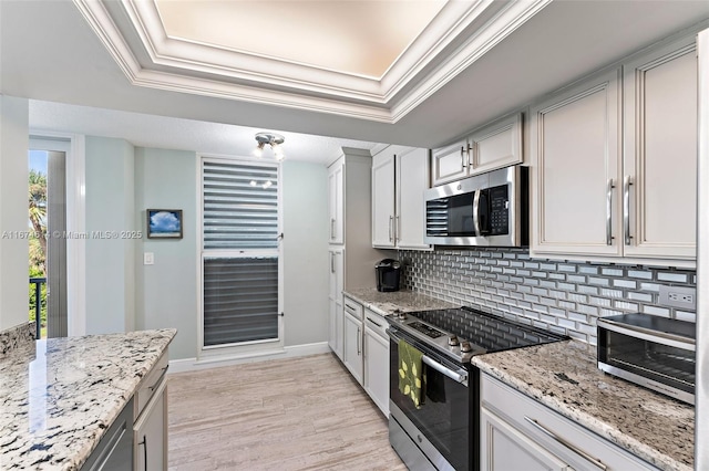 kitchen with stainless steel appliances, light stone counters, a tray ceiling, ornamental molding, and decorative backsplash