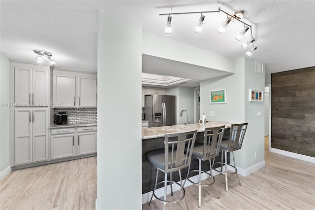 kitchen featuring light hardwood / wood-style flooring, stainless steel fridge, a kitchen breakfast bar, light stone counters, and decorative backsplash