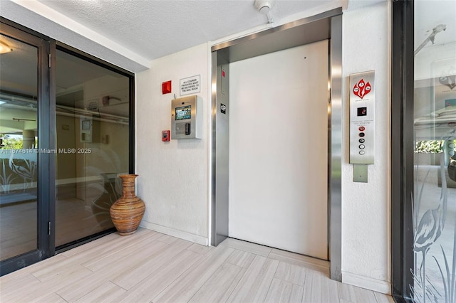 corridor featuring elevator and a textured ceiling