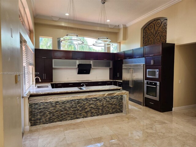 kitchen with a towering ceiling, decorative light fixtures, sink, ornamental molding, and built in appliances