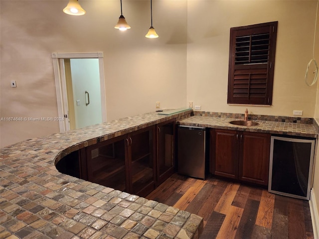 bar featuring stainless steel fridge, dark brown cabinets, dark wood-type flooring, sink, and hanging light fixtures