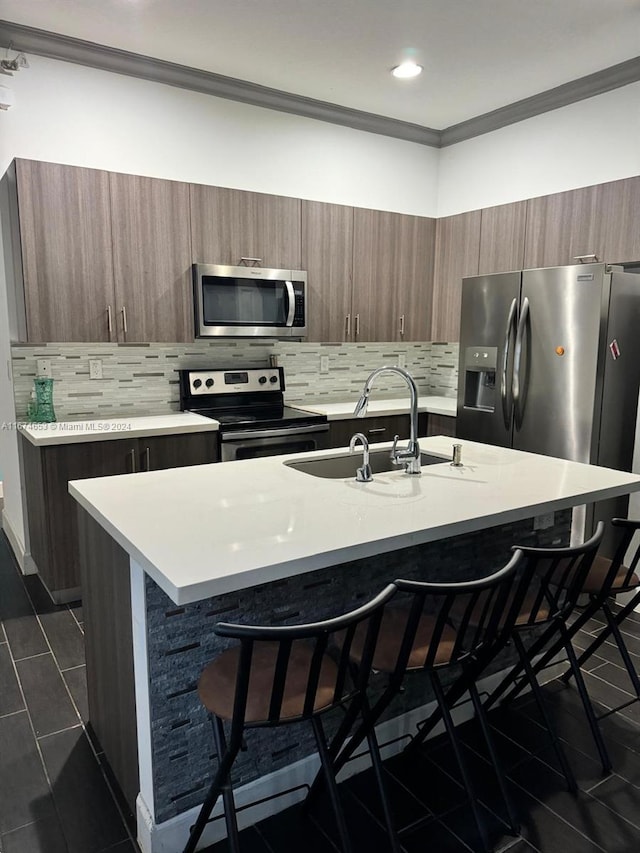 kitchen with an island with sink, stainless steel appliances, a breakfast bar, sink, and crown molding