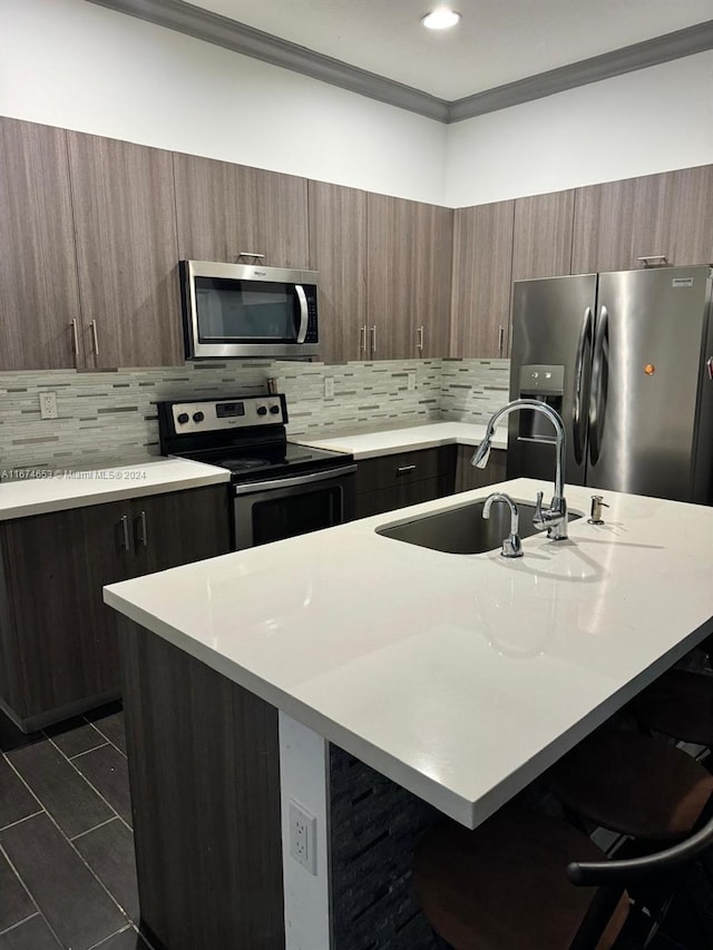 kitchen with a kitchen island with sink, appliances with stainless steel finishes, a kitchen bar, and tasteful backsplash