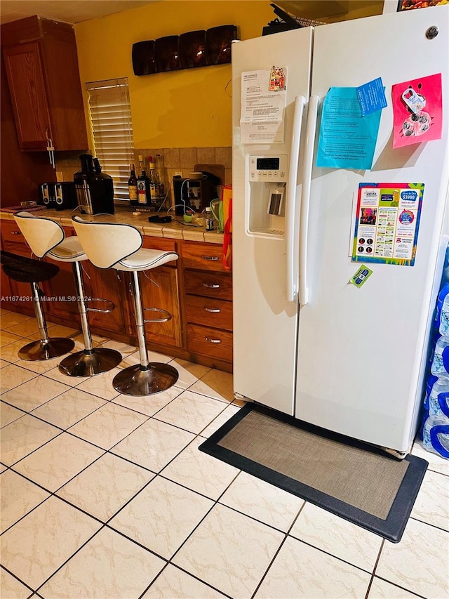 kitchen featuring white fridge with ice dispenser, light tile patterned flooring, and tile counters