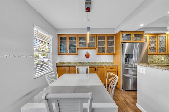 kitchen featuring light stone counters, pendant lighting, backsplash, stainless steel fridge with ice dispenser, and light hardwood / wood-style floors