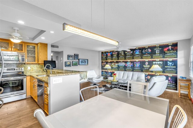 kitchen featuring light hardwood / wood-style flooring, light stone countertops, sink, kitchen peninsula, and appliances with stainless steel finishes