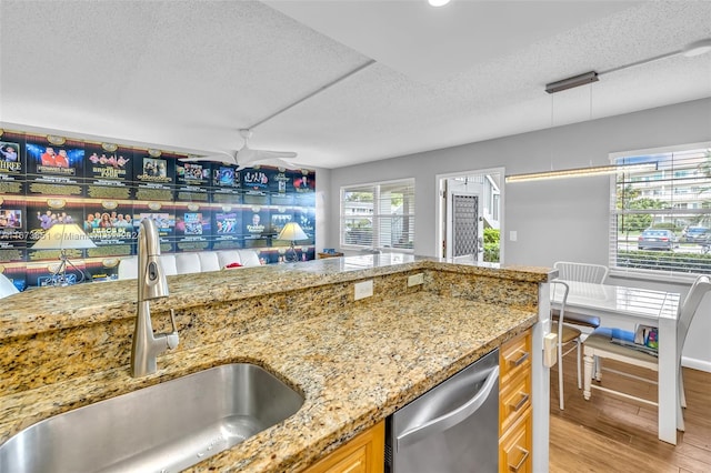 kitchen with dishwasher, sink, light hardwood / wood-style flooring, decorative light fixtures, and a textured ceiling