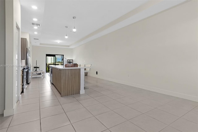 kitchen with decorative light fixtures, a center island, light tile patterned flooring, and a tray ceiling