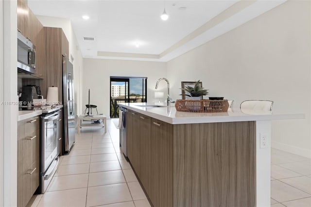 kitchen featuring a kitchen bar, stainless steel appliances, sink, light tile patterned floors, and an island with sink