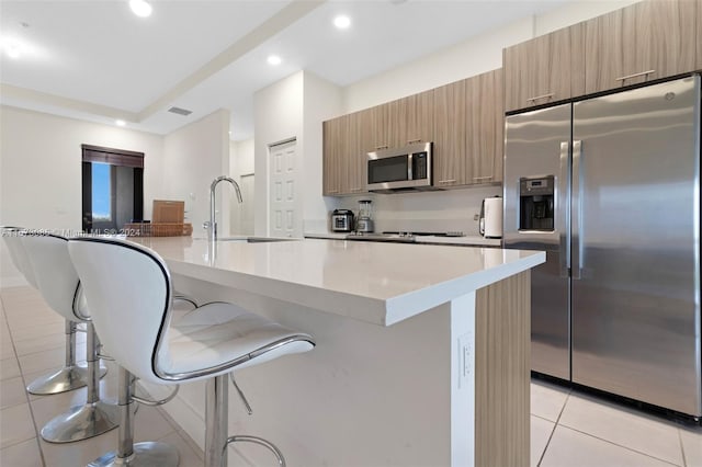 kitchen featuring appliances with stainless steel finishes, a spacious island, sink, a breakfast bar area, and light tile patterned flooring