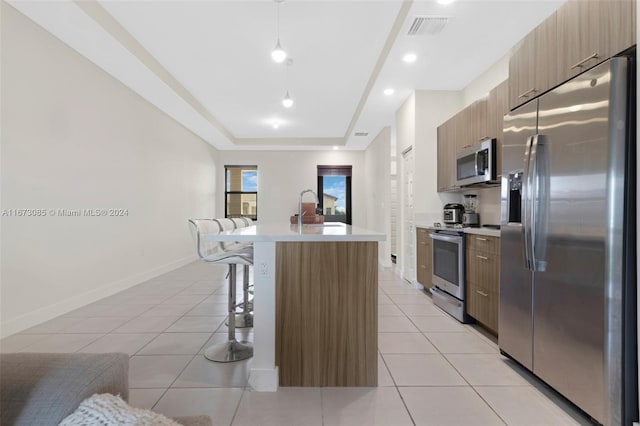 kitchen with a kitchen breakfast bar, a raised ceiling, pendant lighting, a kitchen island with sink, and appliances with stainless steel finishes