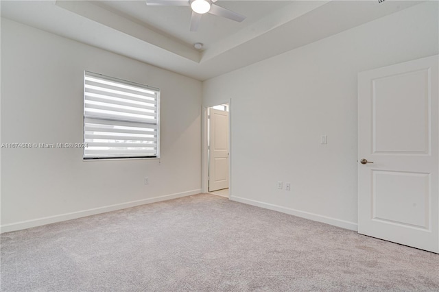 carpeted empty room featuring ceiling fan and a raised ceiling