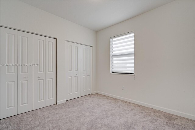 unfurnished bedroom with light carpet and multiple closets